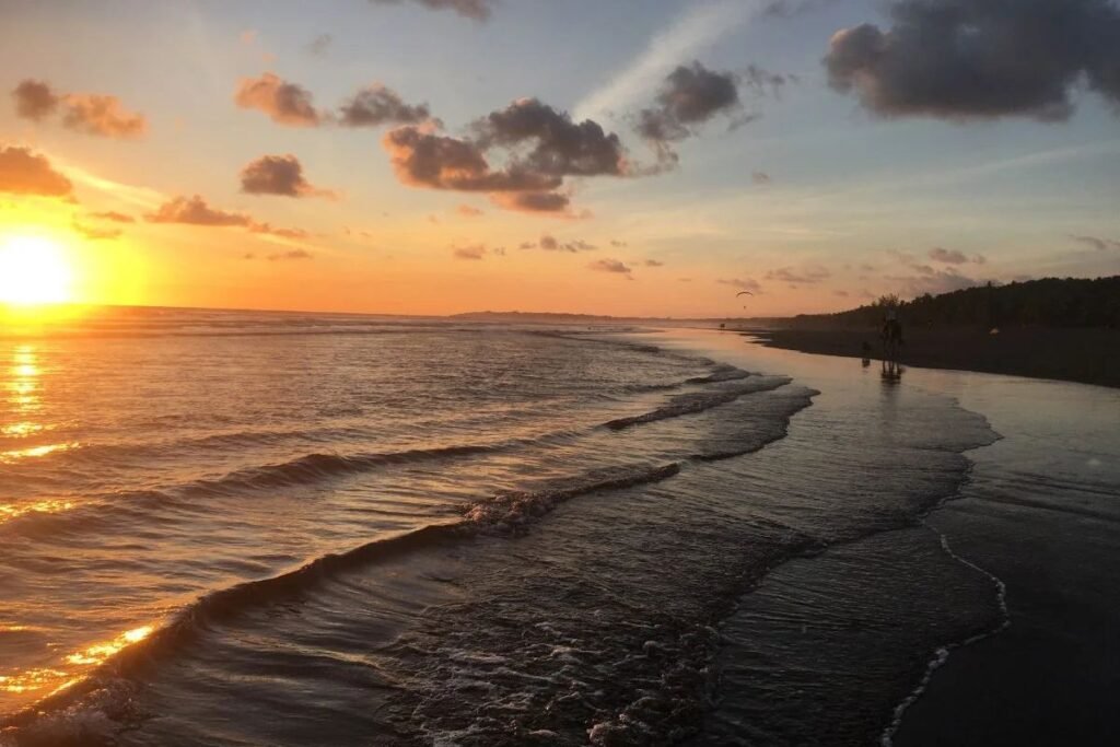 Sunset over a Costa Rica beach with gentle waves, golden reflections, and a colorful sky